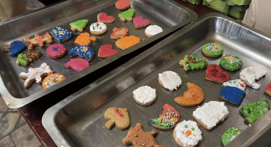 Dva metalna pleha puna šarenih medenjaka u oblicima srca, jelki i zvezda, ukrašenih mrvicama i glazurom.